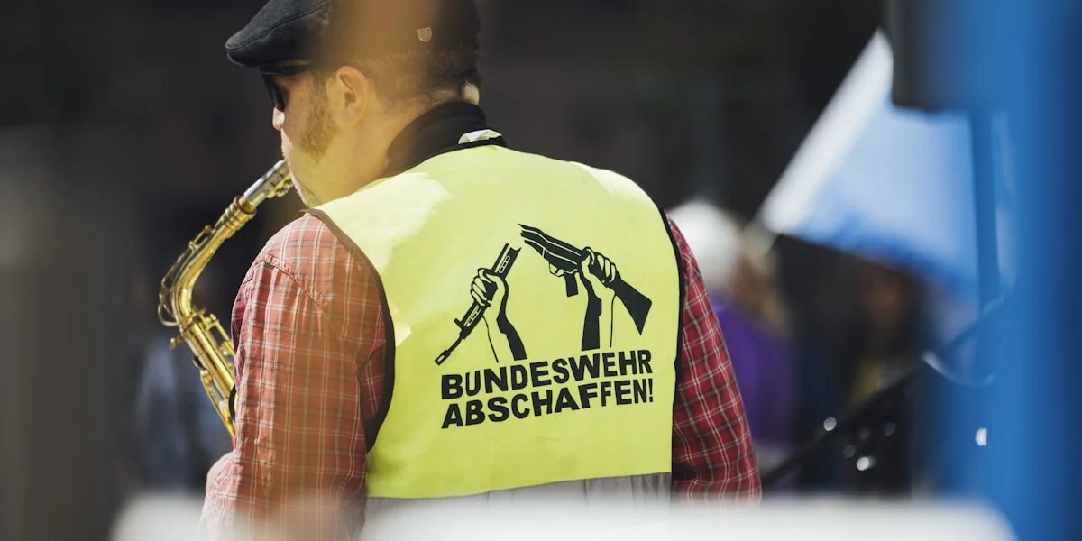 A musician plays saxophone, wearing a protest vest.