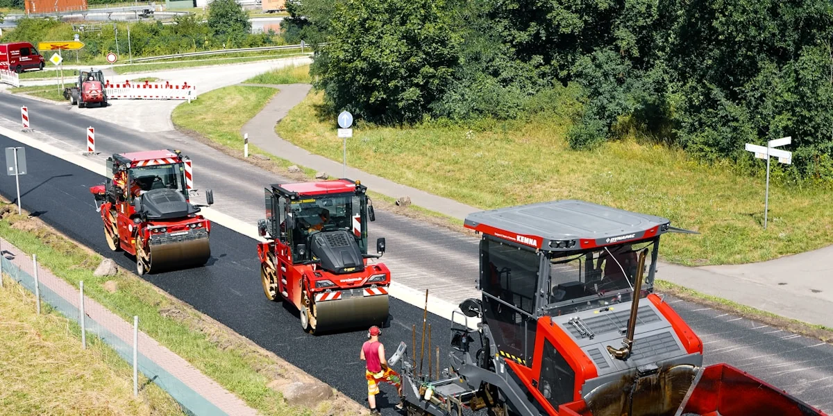 Red road rollers and paver working on new asphalt road.