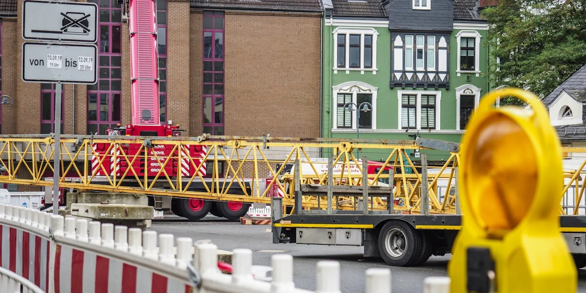 truck loads yellow crane at the back near building